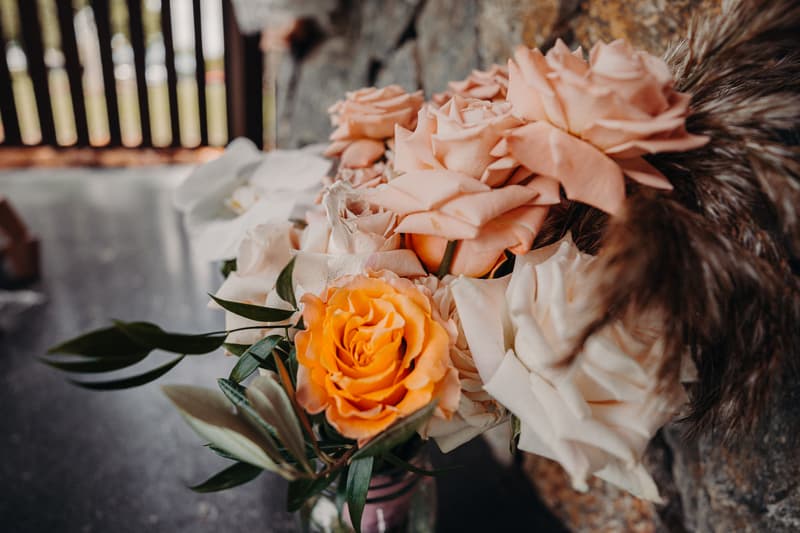 Close-up of a wedding bouquet featuring peach, orange, and white roses with green foliage, placed on a stone surface at Preston Peak Winery Functions Centre.
