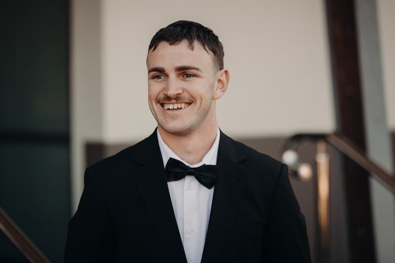 Kyle, the groom, smiles wearing a black tuxedo and bow tie at The Tides — The Water's Edge.