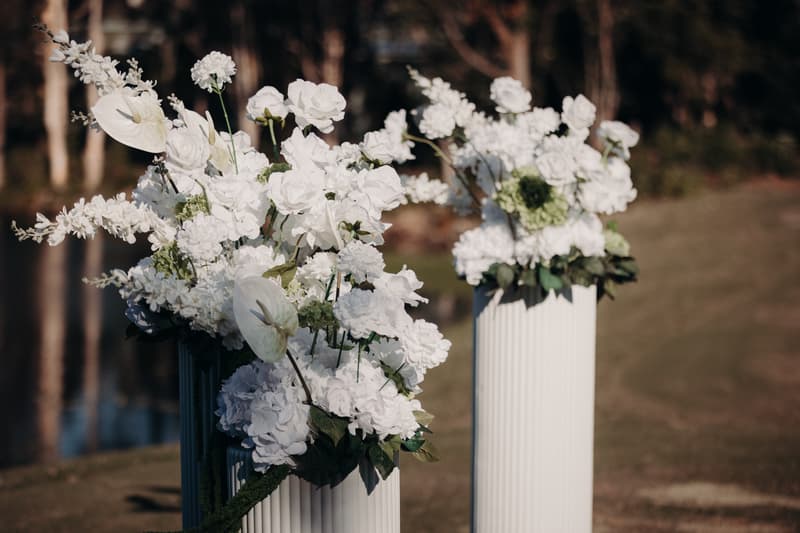 Two white floral arrangements in tall white vases displayed outdoors at The Tides — The Water's Edge.