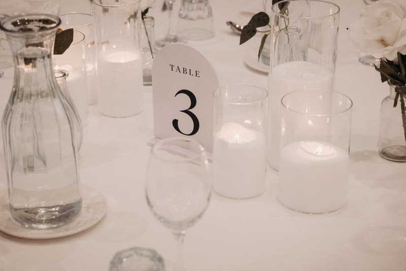 Table 3 at the reception in The Pandanus Room, The Tides, set with glass water carafe, lit candles in glass holders, a table number card, and floral arrangements.