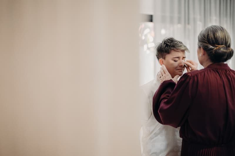 Tiffany is having her makeup adjusted by another woman indoors, possibly during preparation for the wedding.