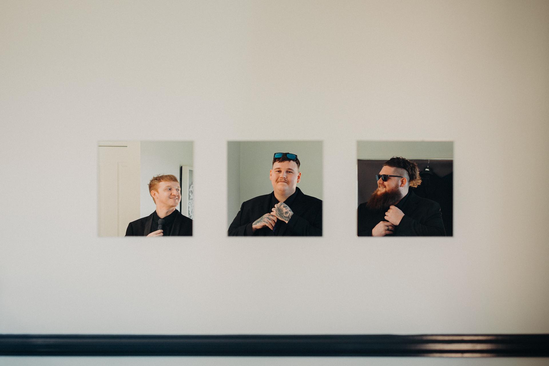 Three groomsmen are individually reflected in three square mirrors mounted on a white wall at Ocean View Estates.