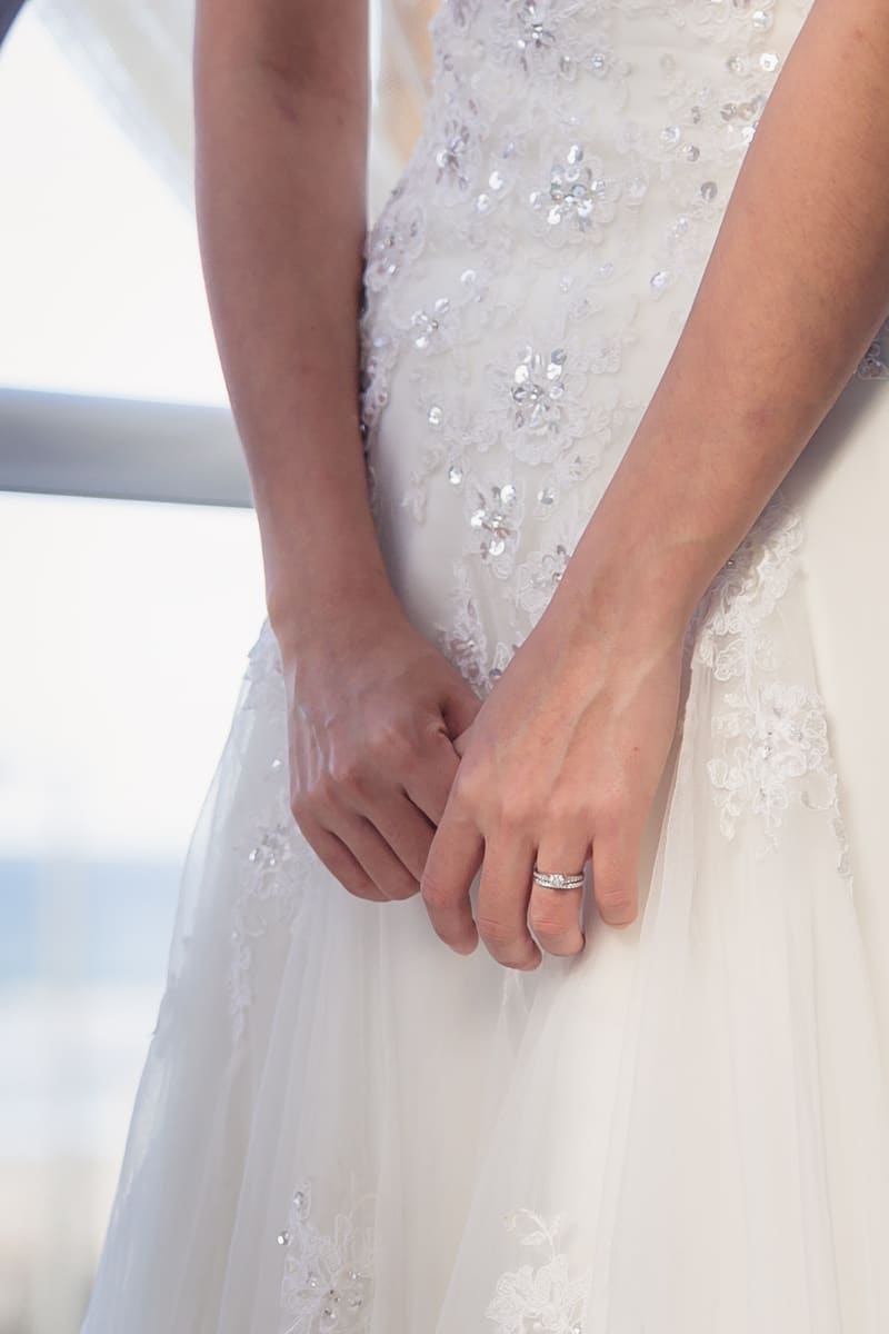 Close-up of the bride's hands clasped in front of her white wedding dress with lace and sequin details. Lead follow-up communication issues by She Said Yes.