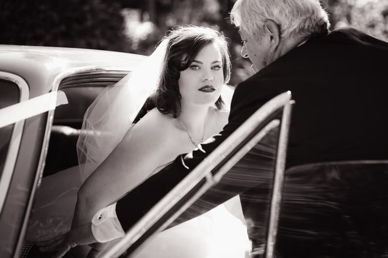 The bride Holly is seated inside a car while an older man, likely her father, leans in through the open door at Kwila Lodge.