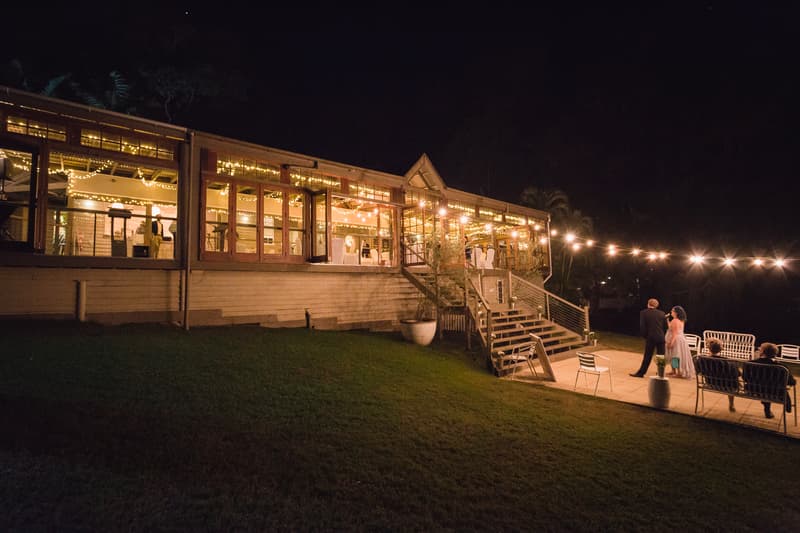 Guests mingle outside Kwila Lodge at night during the wedding reception, with the lodge warmly lit and decorated with string lights.