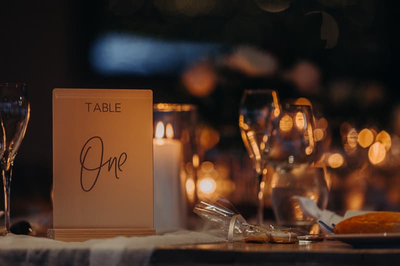 Table One at Preston Peak Winery Functions Centre set with wine glasses, a lit candle, wrapped cookies, and a bread roll on a plate.