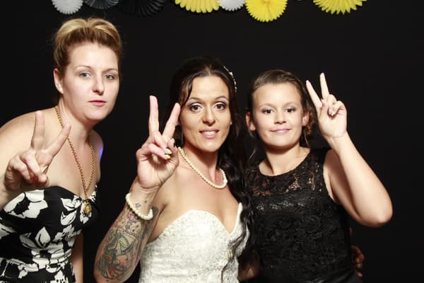 Three guests posing with peace signs in front of a black backdrop with decorative fans.
