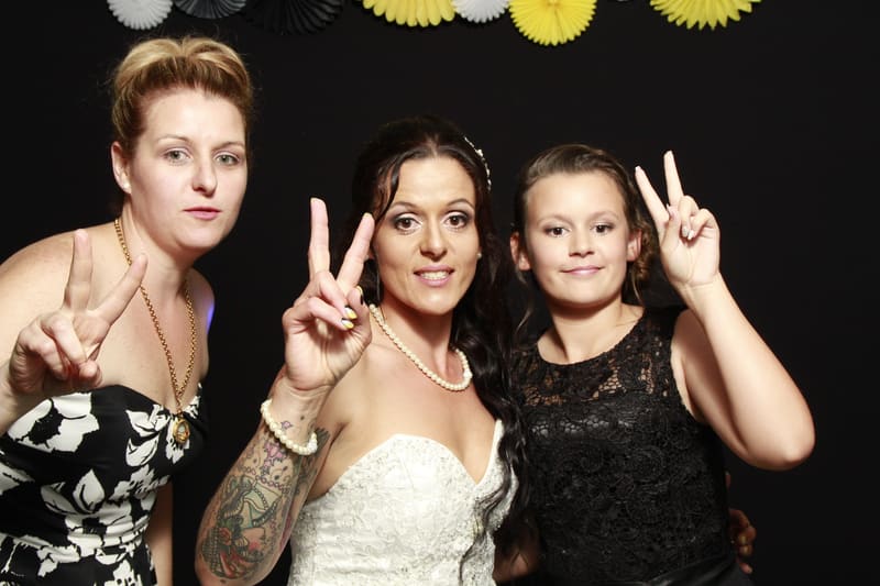Three guests posing with peace signs in front of a black backdrop with decorative fans.
