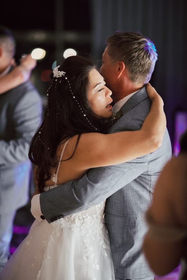 The bride Jheng and groom Dane embrace closely while dancing at their wedding reception in The Pumicestone Room at Sandstone Point Hotel.
