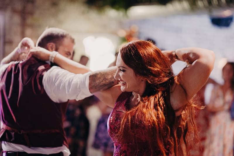 The bride in a red dress and the groom in a white shirt with a dark vest dance together at the reception stage of Sandstone Point Hotel — The Cellar.