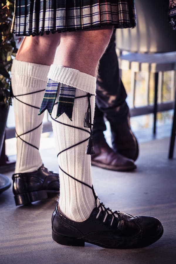 The groom wearing traditional Scottish attire including a kilt, cream knee-high socks with tartan flashes, and black dress shoes at the reception in The Malouf Room, Toowong Rowing Club.