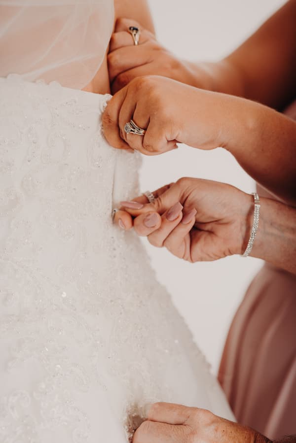 Close-up of hands fastening the back of the bride Emily's wedding dress during preparation.