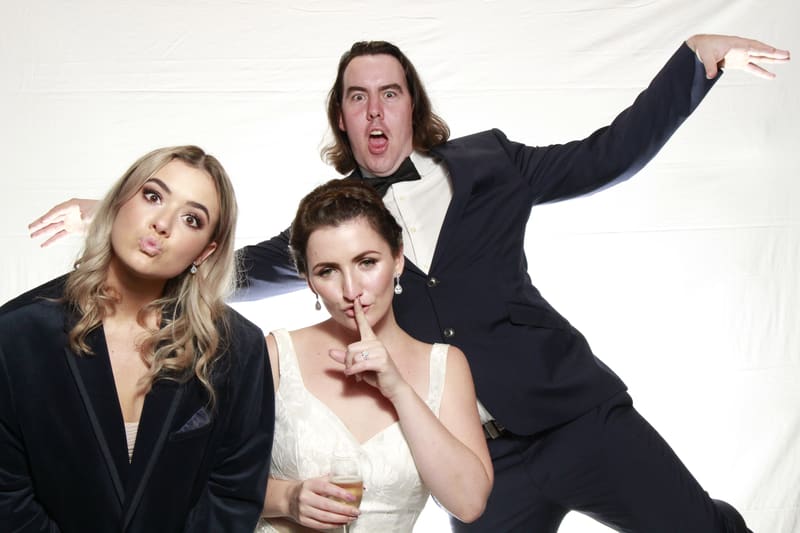 Three guests posing in a photo booth, with playful expressions and props.