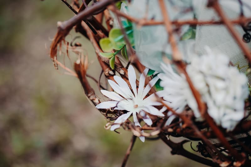 Close-up of white artificial flowers and green leaves intertwined with brown twigs, likely part of wedding decor at Ocean View Estates.