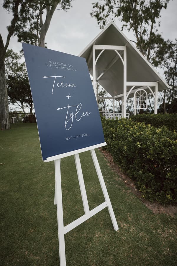 Welcome sign for the wedding of Terion and Tyler dated 21st June 2026 displayed on a white easel on the lawn outside The Pavilion at Sandstone Point Hotel.