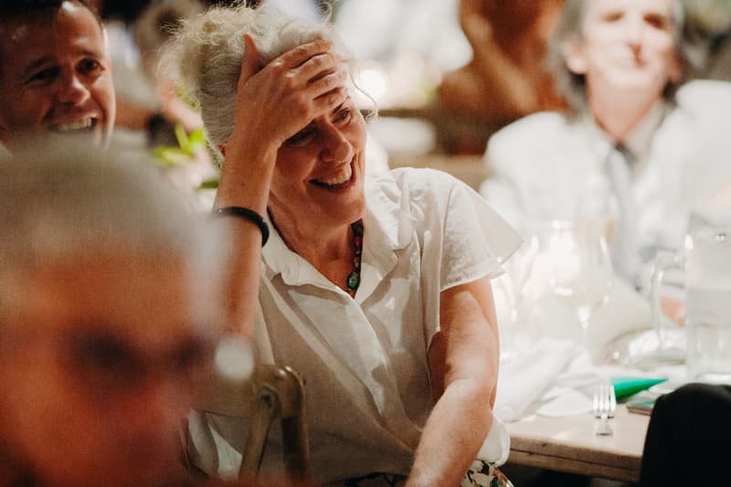 Guests seated at a table during the reception at Preston Peak Winery Functions Centre, with a woman in a white blouse smiling and resting her hand on her forehead.