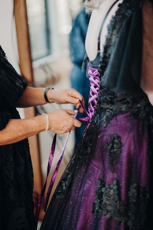 The mother of the bride is fastening the purple lace-up back of the bride Renae's wedding dress at Ocean View Estates.