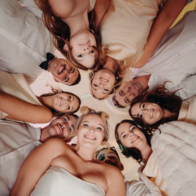 Libby the bride and Kyle the groom with their wedding party form a circle looking down at the camera inside The Tides — The Pandanus Room during the reception.
