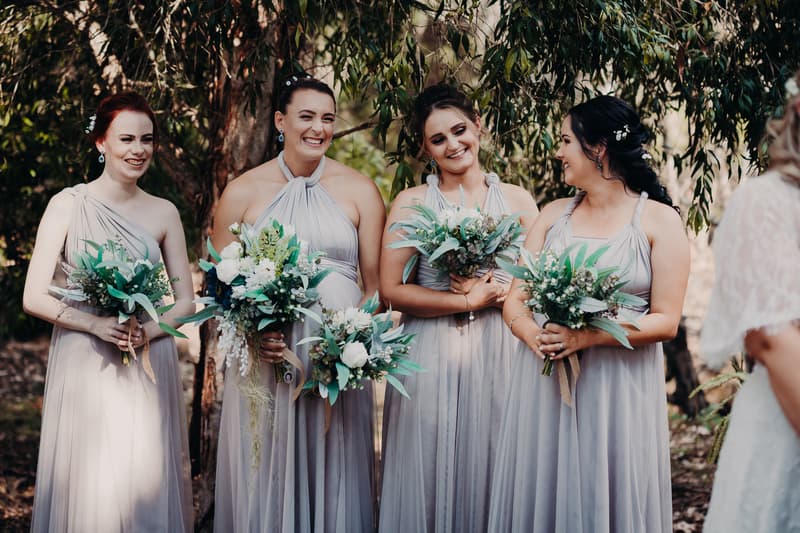 Four bridesmaids stand together outdoors holding bouquets at Ocean View Estates during the ceremony stage.