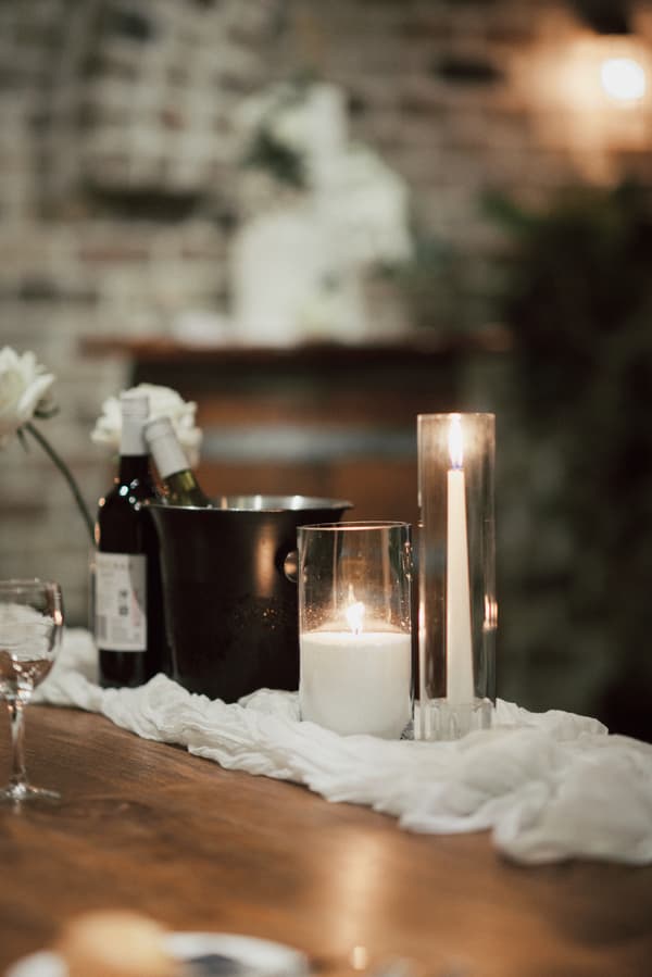 Candles, wine bottles, and an ice bucket arranged on a wooden table with a white cloth at Sandstone Point Hotel — The Cellar during the wedding reception.