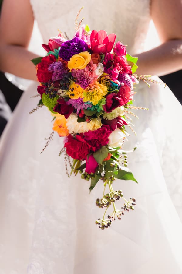 The bride Holly holds a colorful cascading bouquet of flowers in front of her white wedding dress at Kwila Lodge.