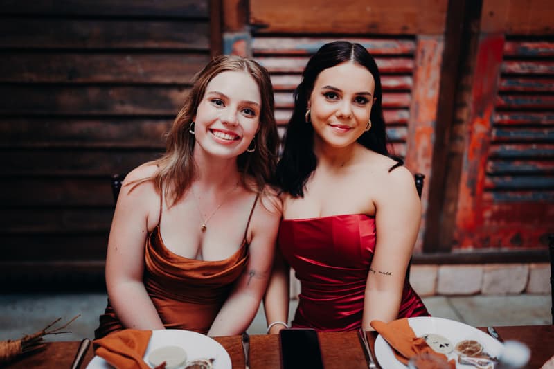 Two female guests sit at a table with plates and napkins at Yabbaloumba Retreat — The Shed during the wedding reception.