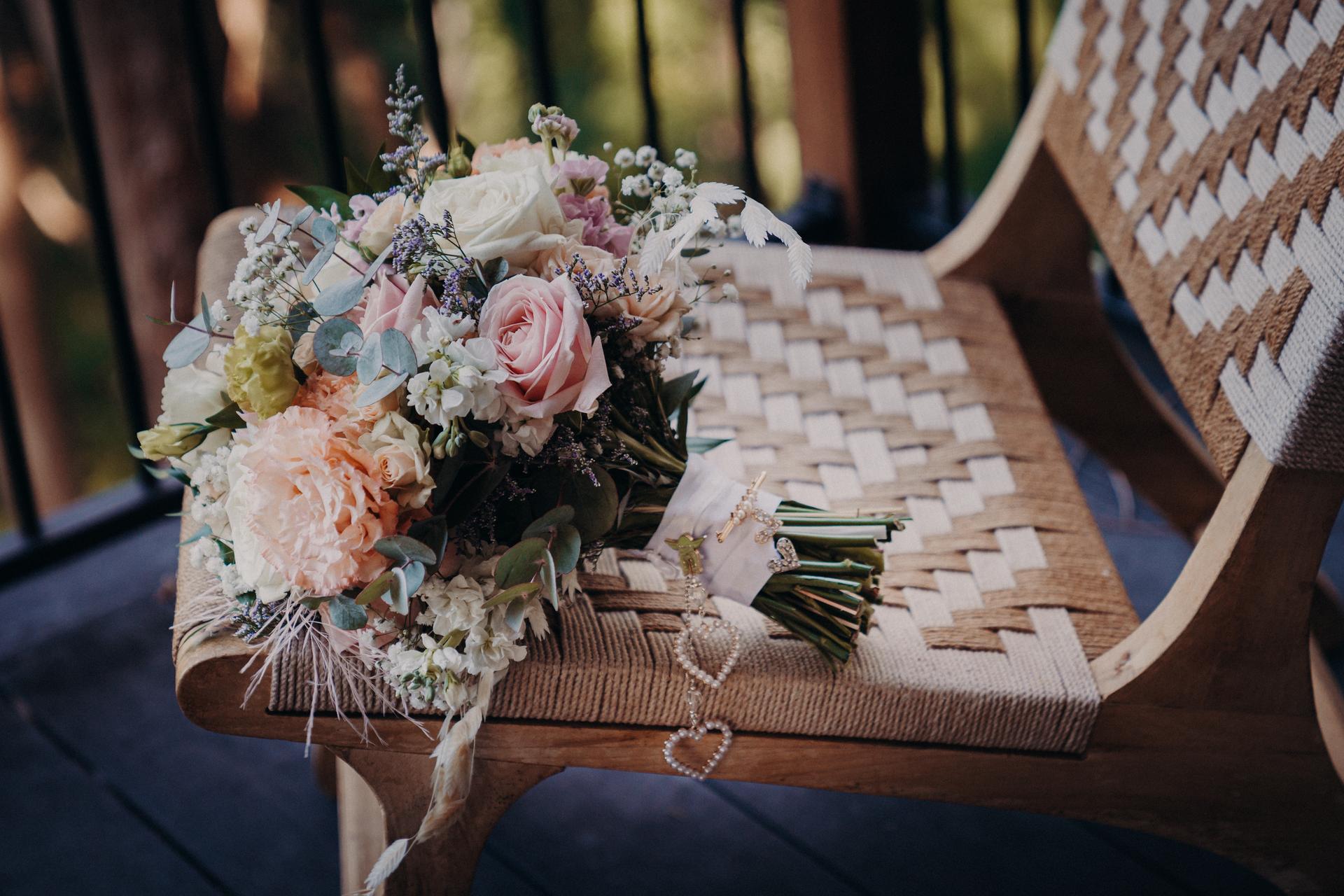 A bridal bouquet with mixed flowers including roses and greenery rests on a woven wooden chair at Sandstone Point Hotel.