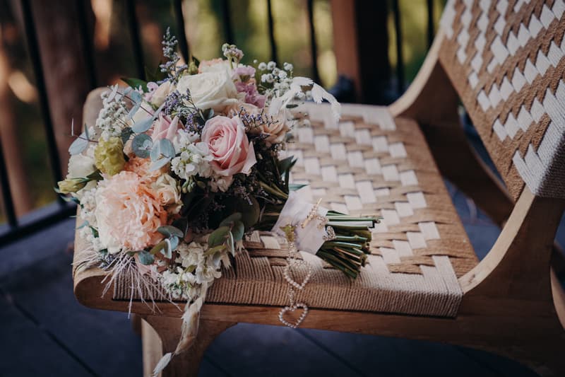 A bridal bouquet with mixed flowers including roses and greenery rests on a woven wooden chair at Sandstone Point Hotel.