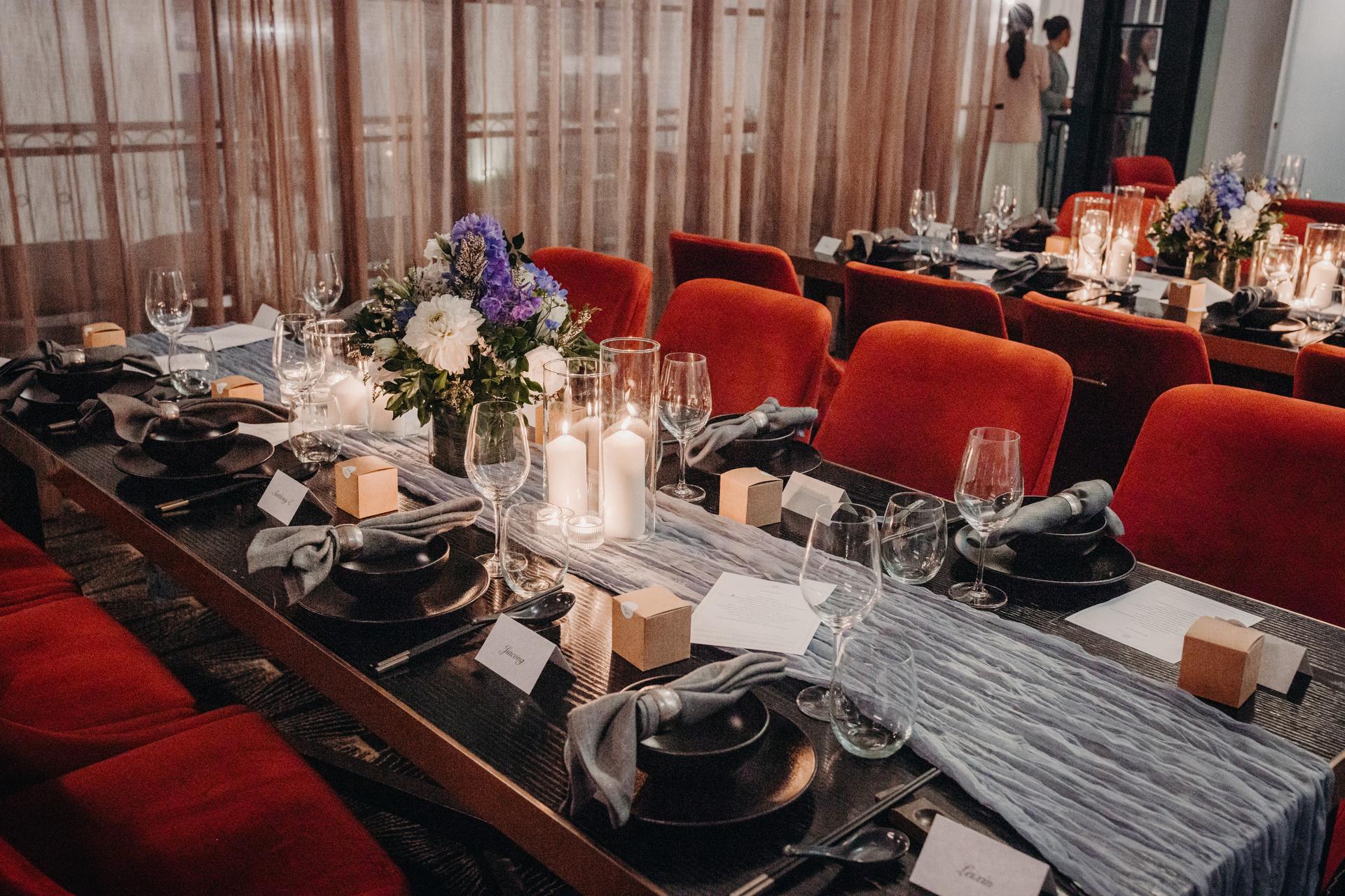Table set for wedding reception at Donna Chang with red chairs, floral centerpieces, candles, glassware, and place cards.