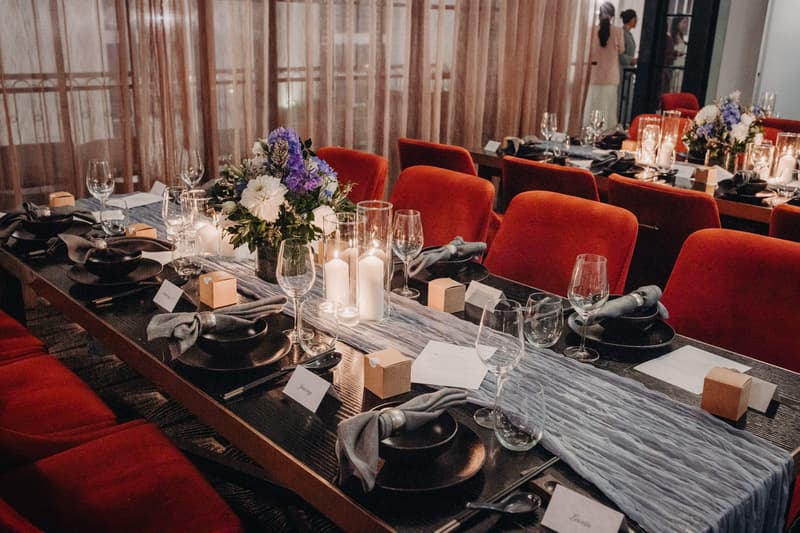 Table set for wedding reception at Donna Chang with red chairs, floral centerpieces, candles, glassware, and place cards.