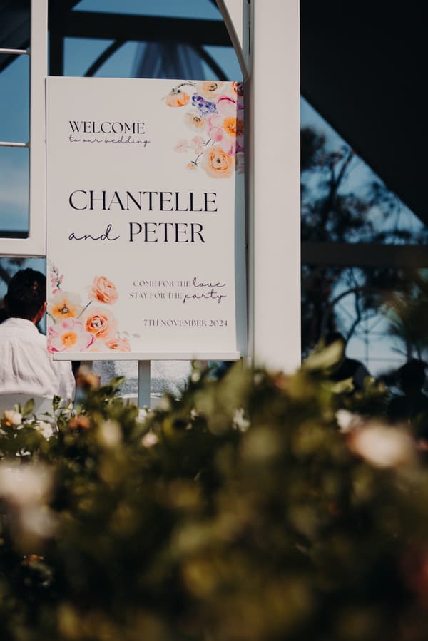 Wedding welcome sign for Chantelle and Peter at Sandstone Point Hotel — Pavilion, dated 7th November 2024, with floral decorations and partially visible guests in the background.