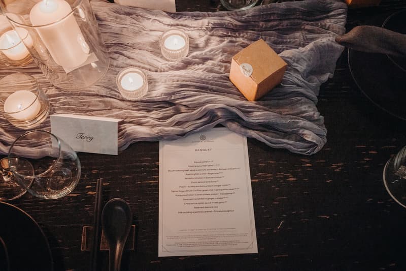 Table setting at Donna Chang with a banquet menu, candles, a place card labeled 'Terry', a small gift box, and glassware on a dark wooden table with a textured cloth runner.