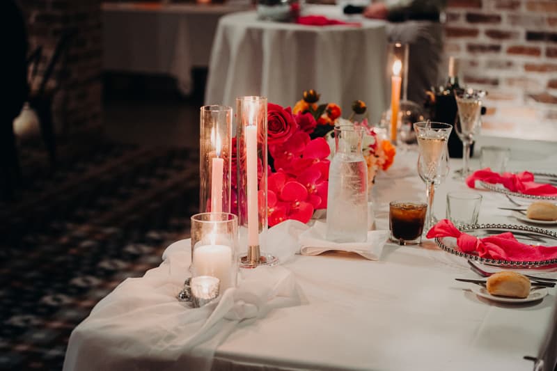 Table setting at the Sandstone Point Hotel — Cellar with lit candles, pink floral centerpiece, glassware, and plates with pink napkins and bread rolls.