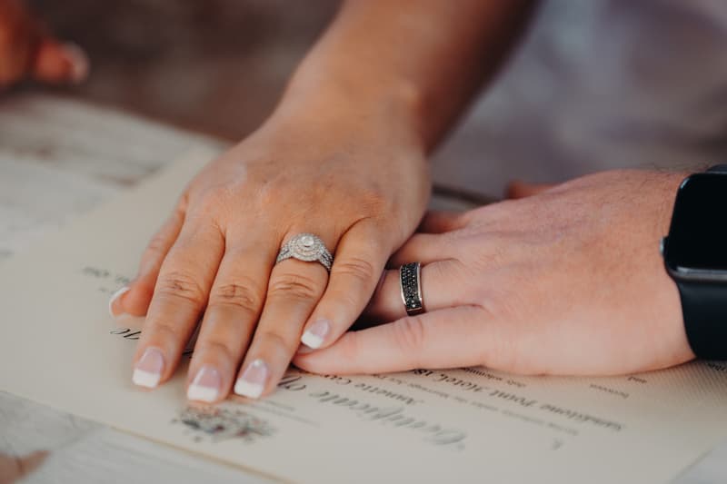 Close-up of the bride Chantelle's and groom Peter's hands resting on a wedding certificate at Sandstone Point Hotel — Pavilion, showing their wedding rings.