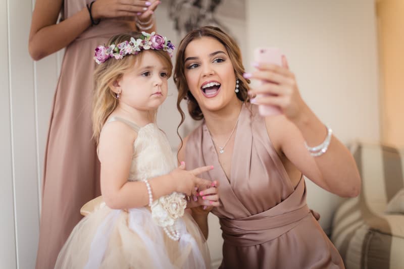 A bridesmaid in a mauve dress takes a selfie with a flower girl wearing a cream dress and floral headband at Novotel Sunshine Coast Resort.