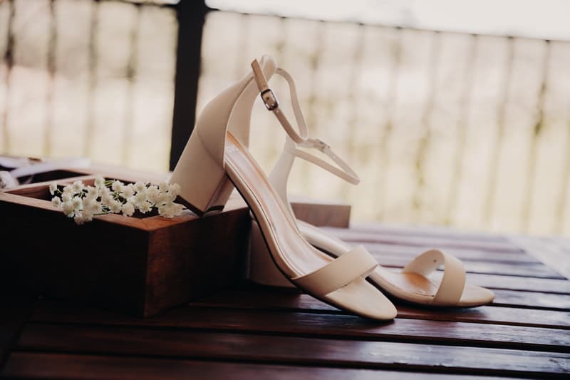 A pair of beige bridal heels resting on a wooden surface next to a wooden box with small white flowers at Ocean View Estates.