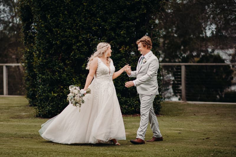 Chloe and Brodie hold hands and smile at each other outdoors at Sandstone Point Hotel during their couple portraits session.