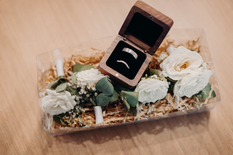 Wedding rings in a wooden box surrounded by white floral boutonnieres on a wooden surface at Sandstone Point Hotel.
