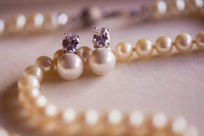 Close-up of pearl earrings with diamond studs resting on a pearl necklace on a soft surface.