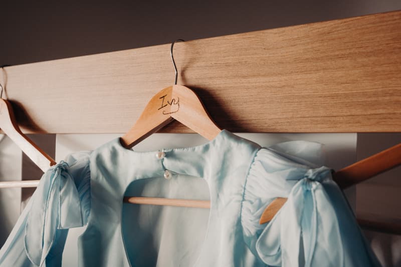 A light blue bridesmaid dress hanging on a wooden hanger labeled 'Ivy' on a wooden rail.