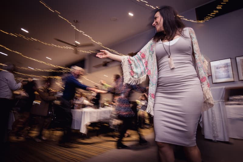 A female guest dances at the reception in The Malouf Room at Toowong Rowing Club, with other guests dancing and mingling in the background under string lights.