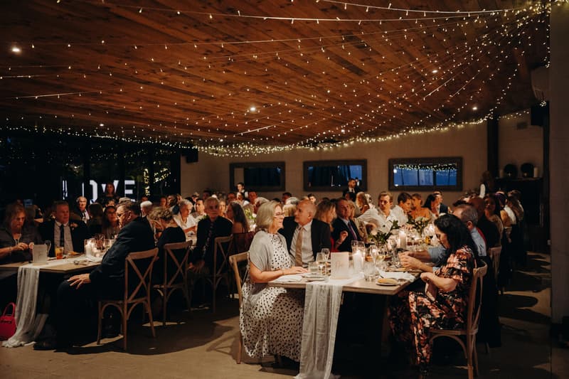 Wedding guests seated at long tables under string lights at Preston Peak Winery Functions Centre during the reception.