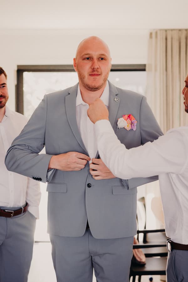 The groom Arran is having his suit jacket adjusted by a groomsman while another groomsman looks on at Sandstone Point Hotel.