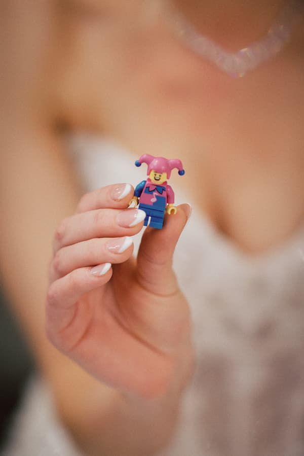The bride at Sandstone Point Hotel — The Pumicestone Room holds a small LEGO jester figurine close to the camera, showing her French manicured nails and part of her wedding dress.