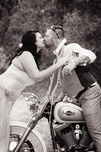 Bride Kelly and groom Shane kiss while Shane leans on a Harley Davidson motorcycle outdoors. Photo booth hire Sunshine Coast by She Said Yes.