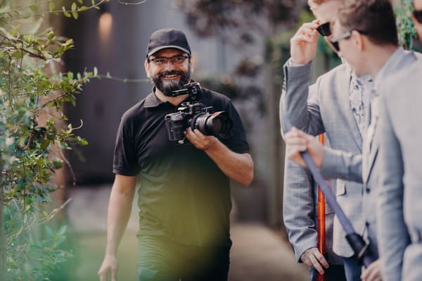 Roman walking with a small cinema camera and smiling to the groomsmen