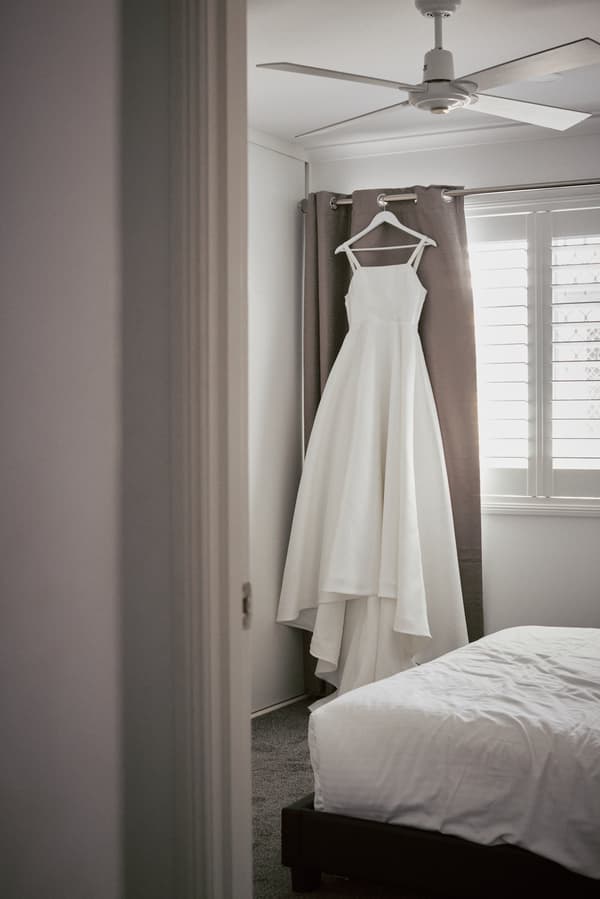 The bride's wedding dress hangs on a hanger in a bedroom at Sandstone Point Hotel.