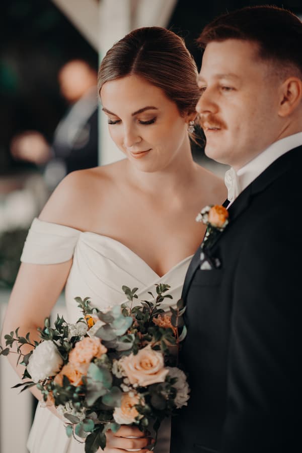 Courtney the bride and Liam the groom stand close together at Tiffany's Maleny, with Courtney holding a bouquet of flowers.