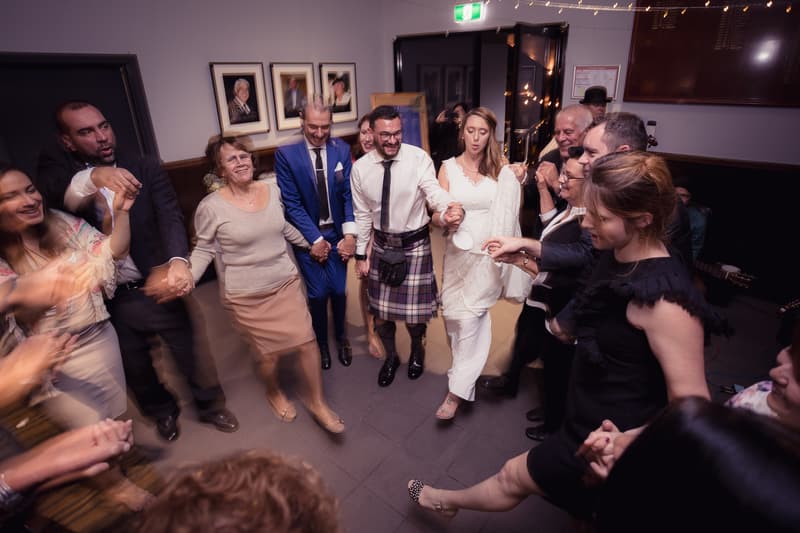 Francesca the bride and Ben the groom hold hands and dance in a circle with guests at the reception in The Malouf Room at Toowong Rowing Club.