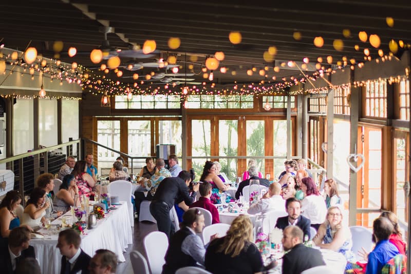 Guests seated at tables inside Kwila Lodge during the wedding reception, with string lights hanging from the ceiling and large windows letting in natural light.